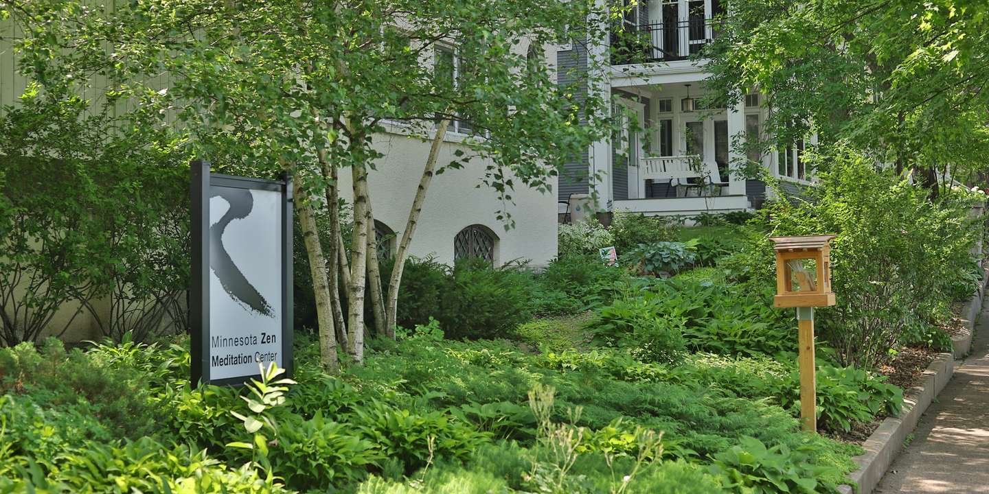 The center’s sign, a black brush stroke above the words Minnesota Zen Meditation Center, among birch trees and hostas in front of the white building
